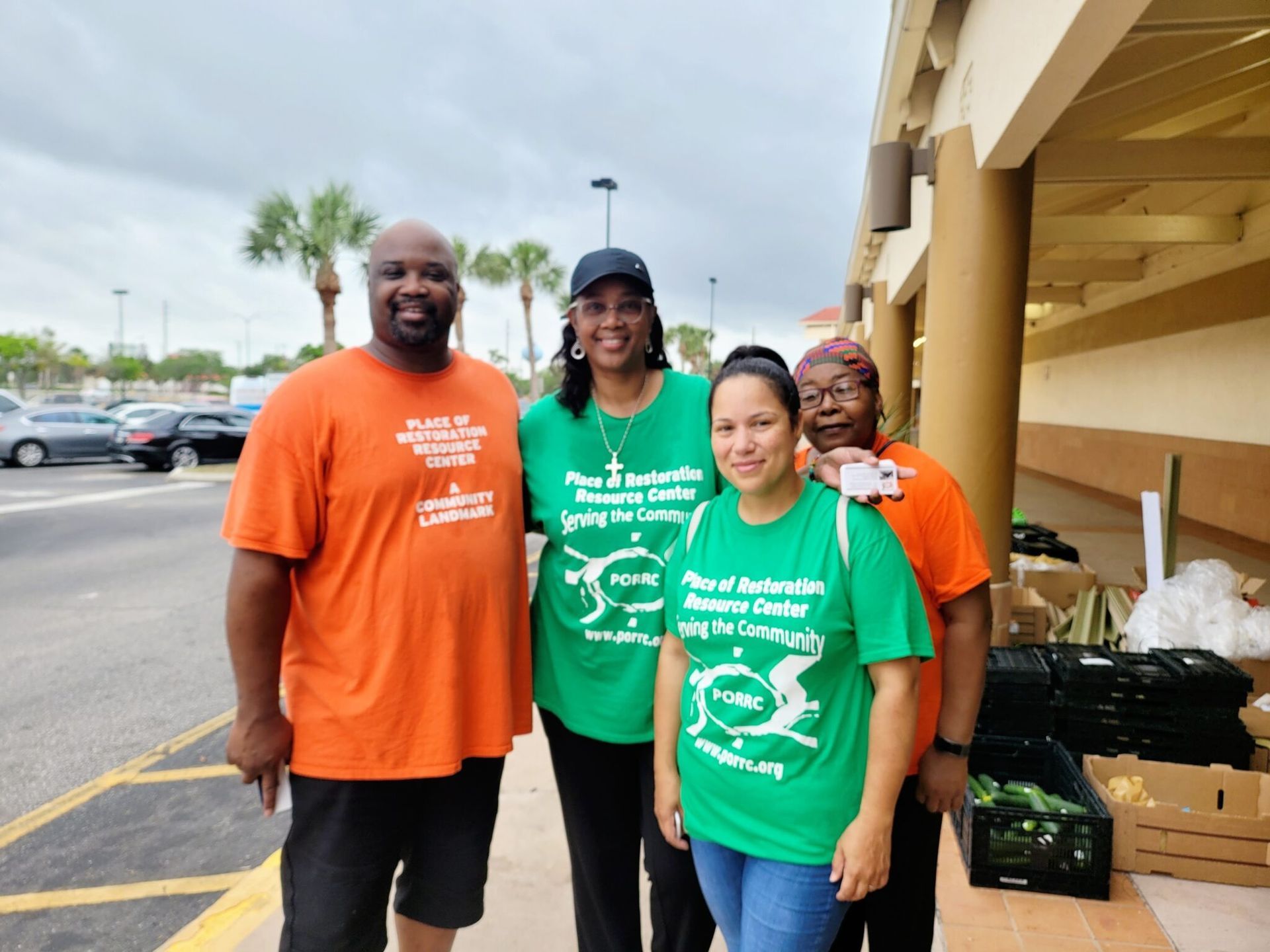 Four people wearing green and orange shirts standing outside a store. They are smiling.