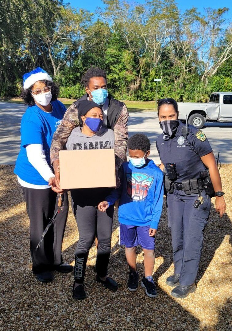 Family and police officer pose outdoors, holding a sign. All wear face masks; some in blue.