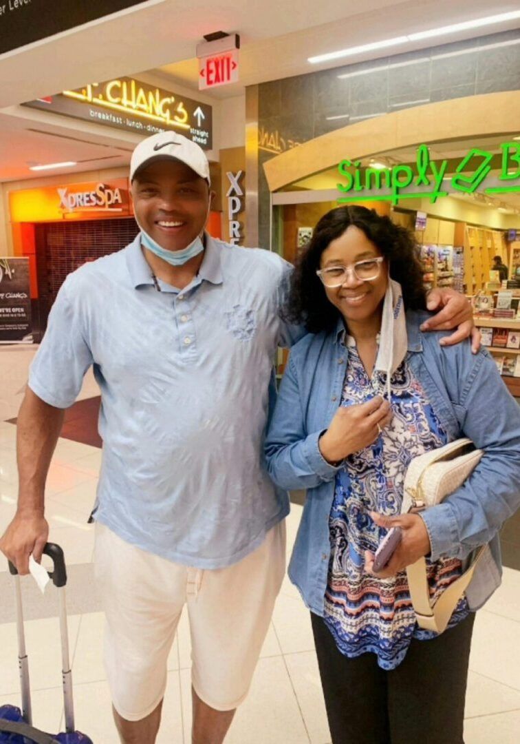 A man and woman smiling in an airport. Man has arm around woman, both wearing masks.