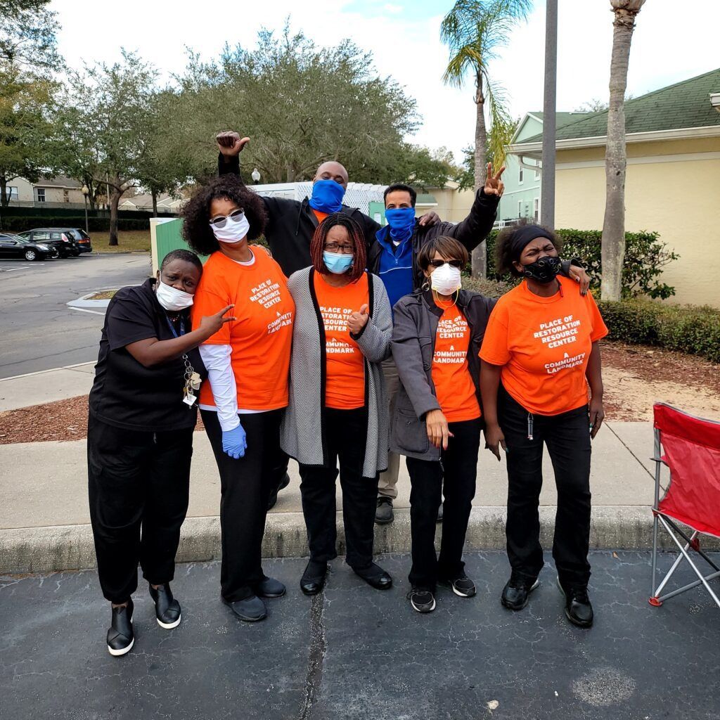 Group of people in orange shirts, some wearing masks, posing outdoors.