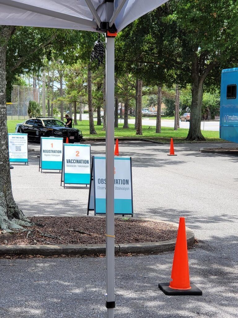 A parking lot with signs for COVID-19 testing, tent pole in foreground.