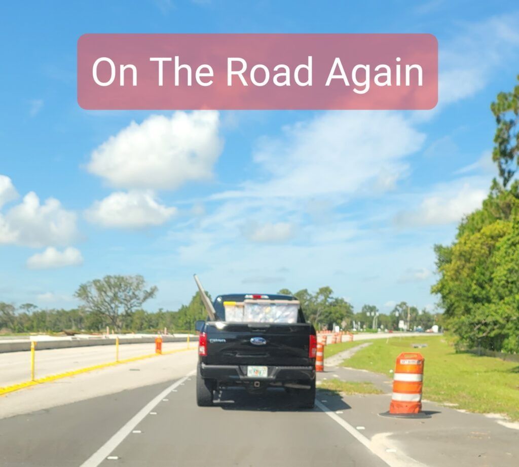 Black pickup truck driving on a sunny road, text reads "On The Road Again".