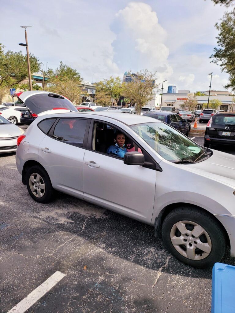 Silver SUV with open trunk, a person smiling from driver's seat. Parked in a lot, sunny day.
