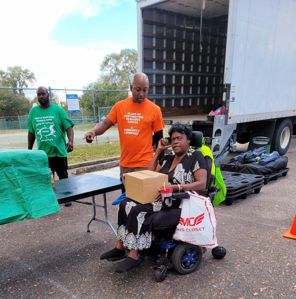 People unloading supplies from a truck; a person in a wheelchair receives a box.