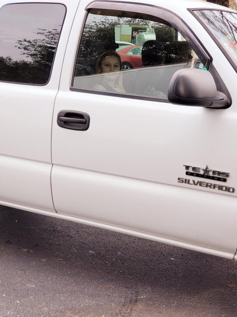 White Silverado truck with a person inside looking out the window.