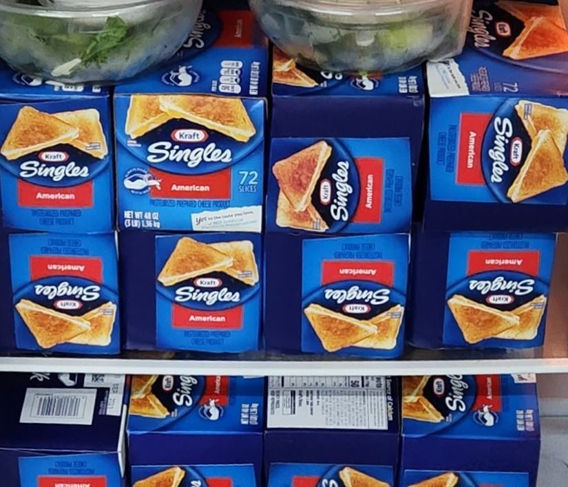 Boxes of Kraft Singles American cheese, stacked in a refrigerator. Blue boxes with grilled cheese sandwich illustrations.