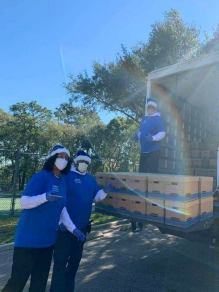 People in blue shirts and hats unloading boxes from a truck. Sunny day.