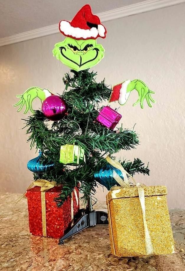 Grinch-themed Christmas tree with Grinch face, ornaments, presents, and outstretched arms.
