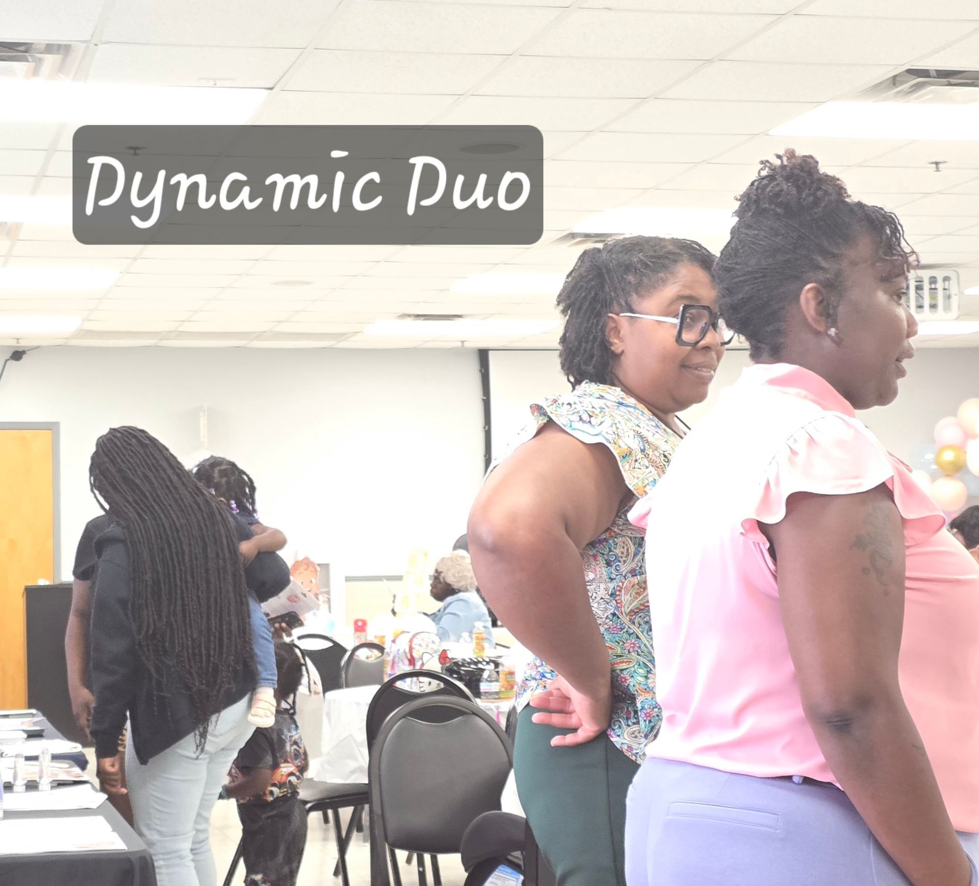 Two people standing in a bright room with the words “Dynamic Duo” overlaid in the corner