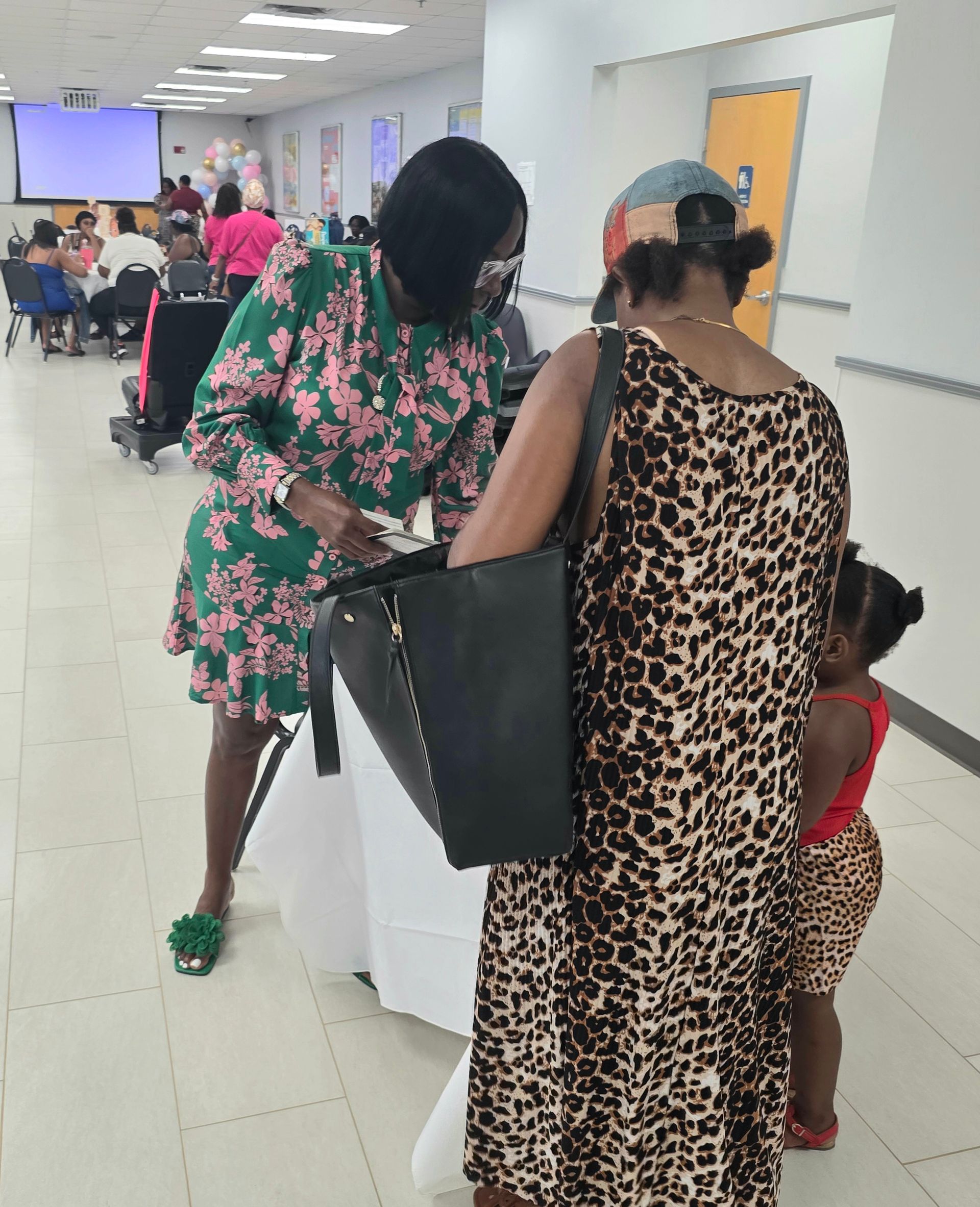 People standing in a bright hallway, one with a large black bag, another holding a child.