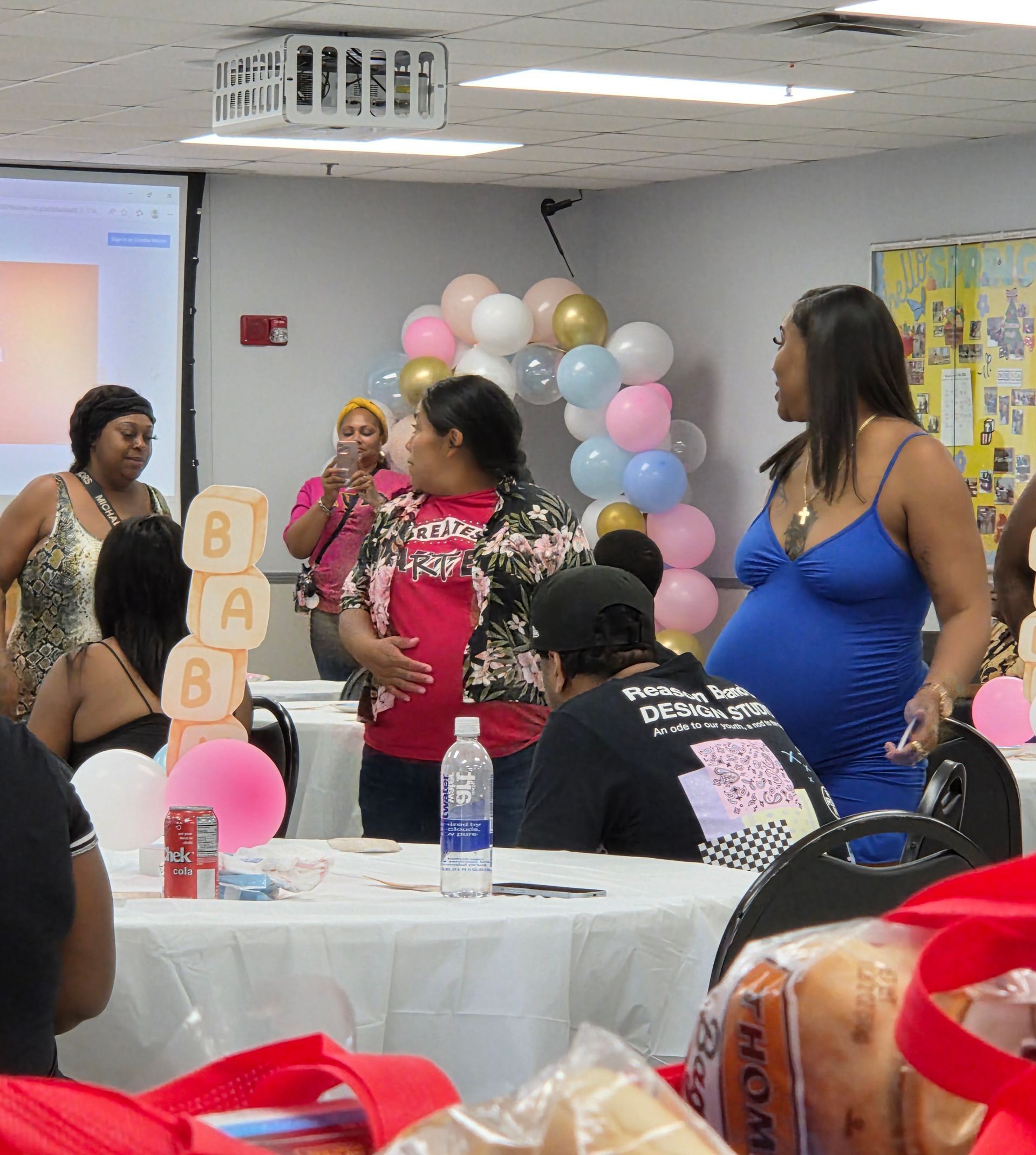 People standing and chatting at a birthday party with pastel balloon decorations and a gift table.