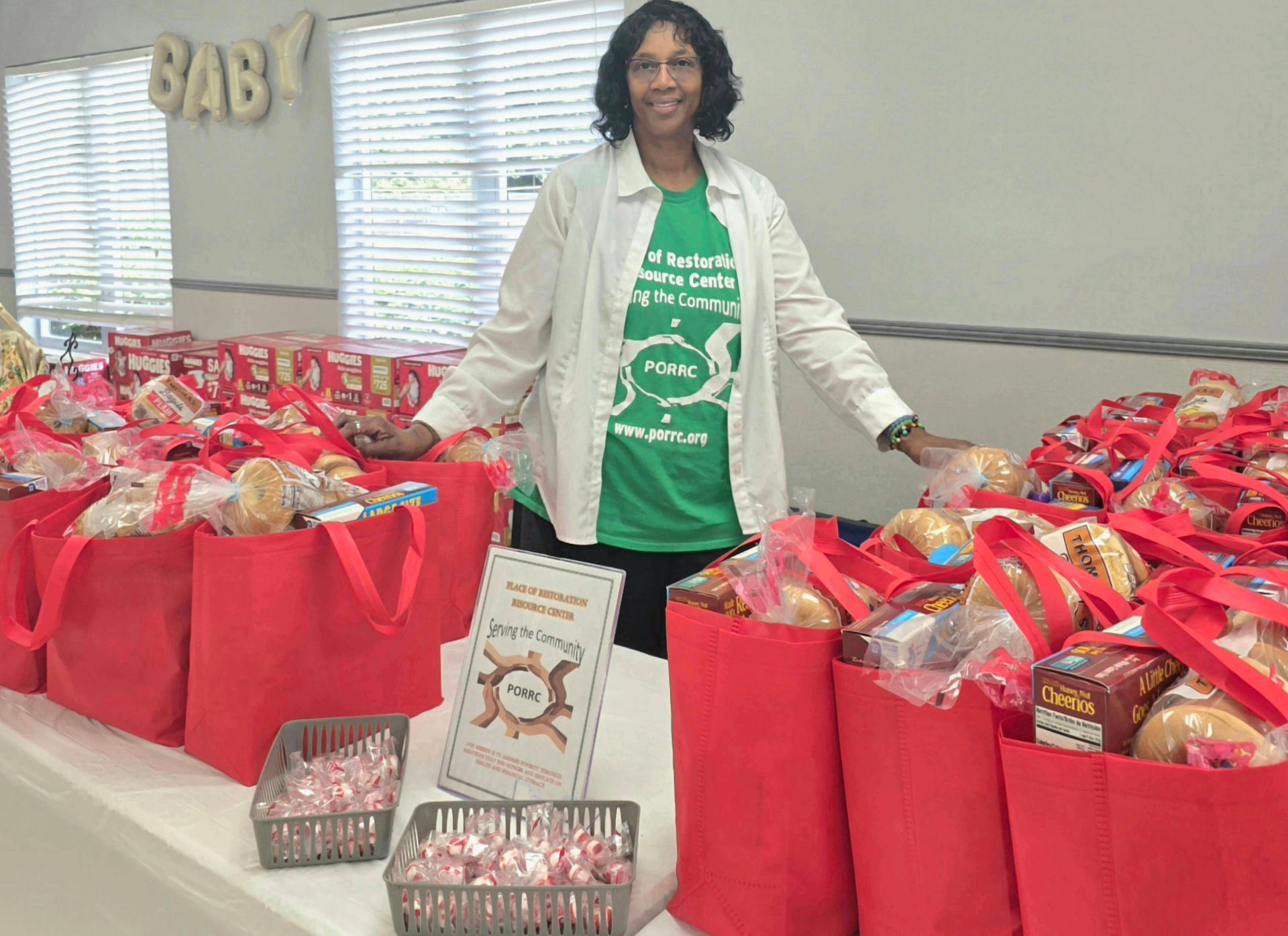 Woman standing behind tables of red gift bags at a BABY shower event