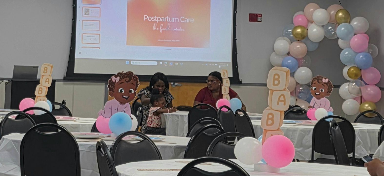 Baby shower table with balloons, “BABY” blocks, and a projected presentation on the wall