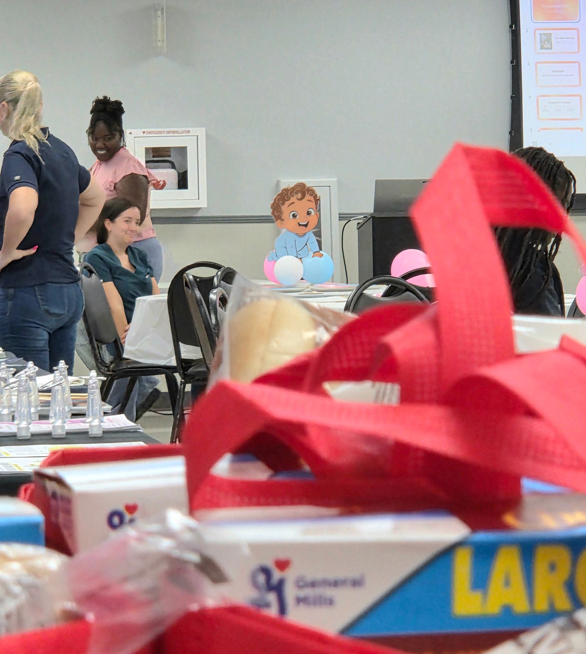 Indoor gathering with people seated at tables and a cartoon child cutout in the background