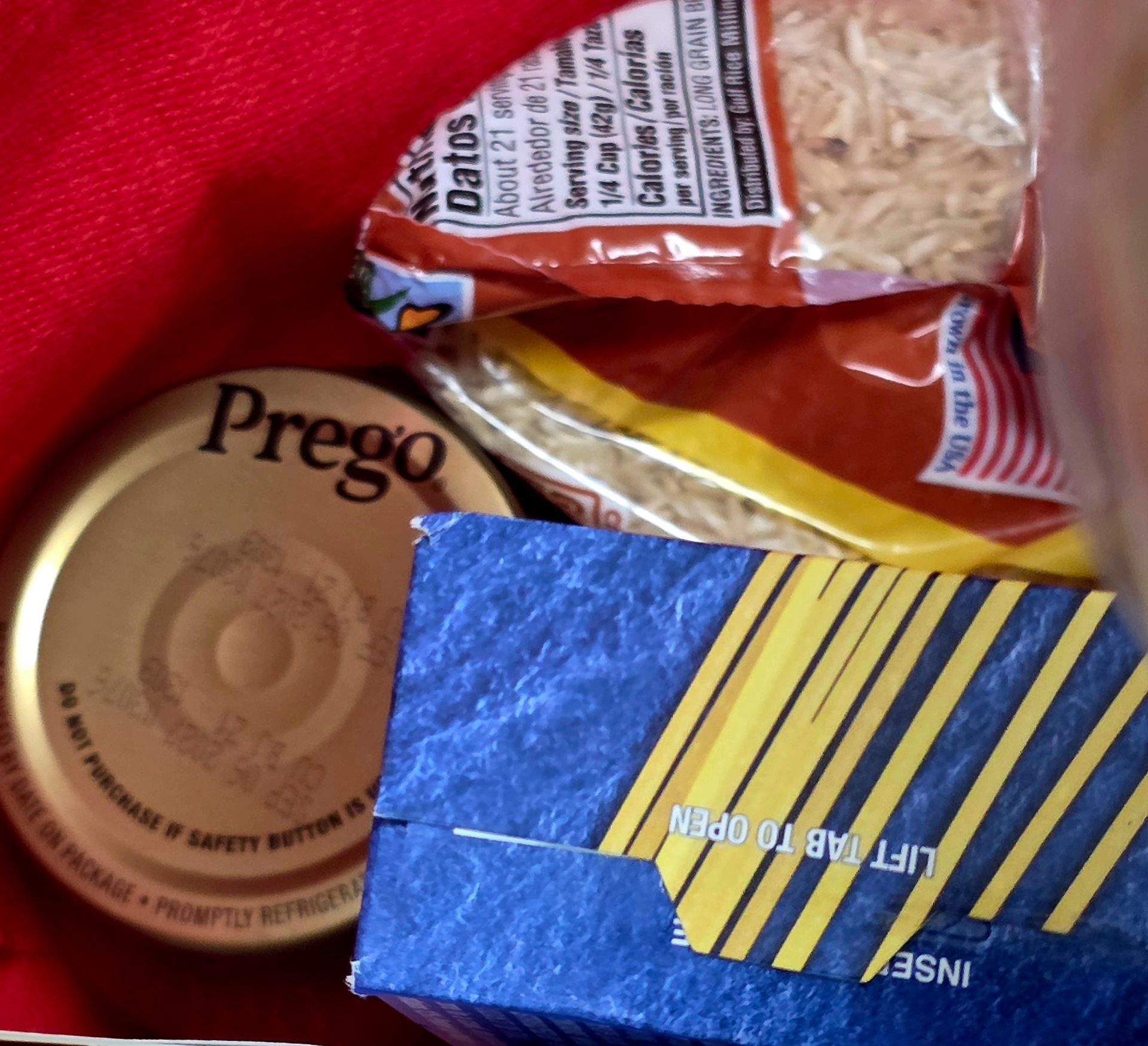 A red bag holding a Prego sauce jar, a blue box, and a packet of bread