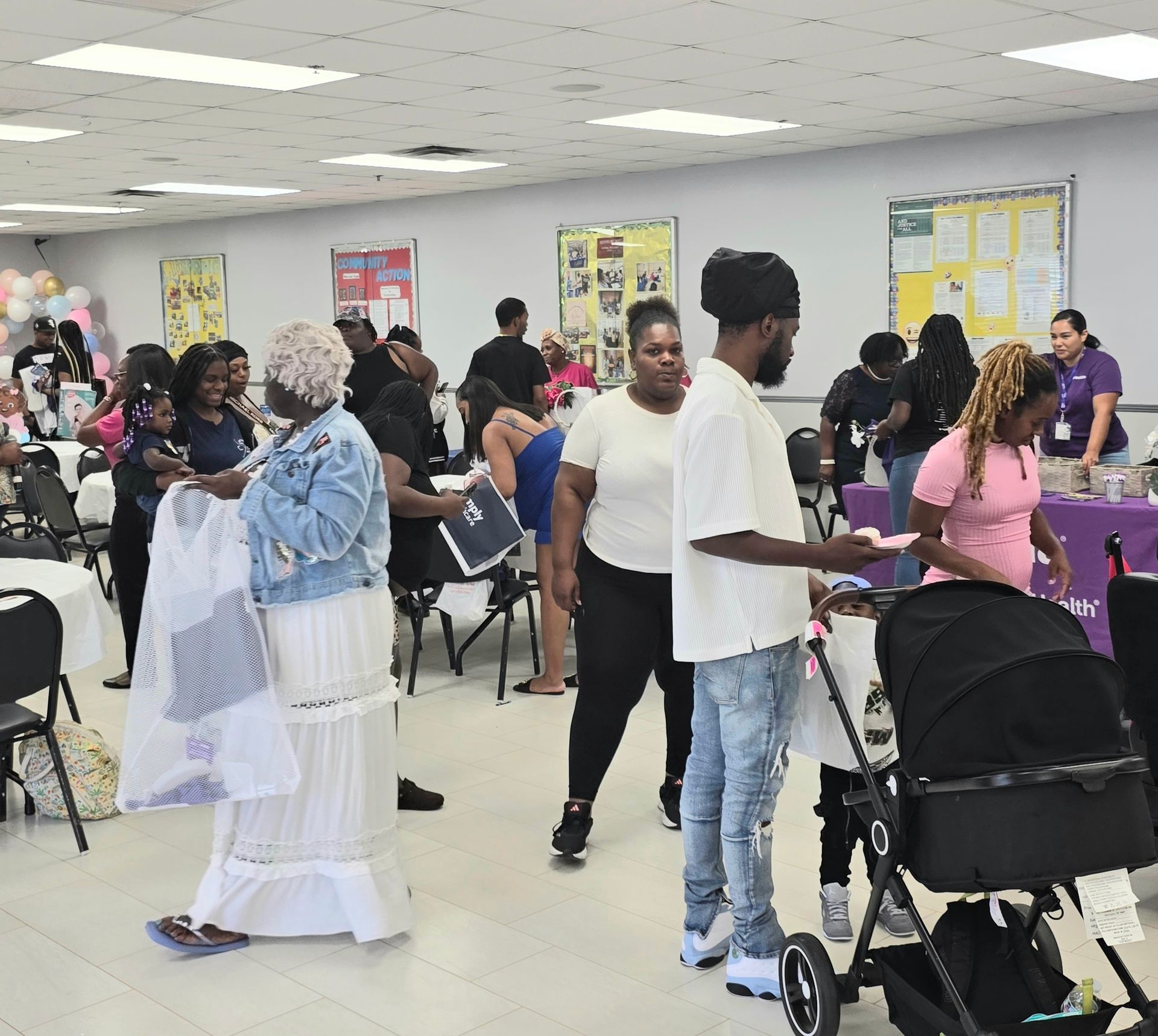 People socializing in a community room, with chairs, posters, and a stroller in the foreground.