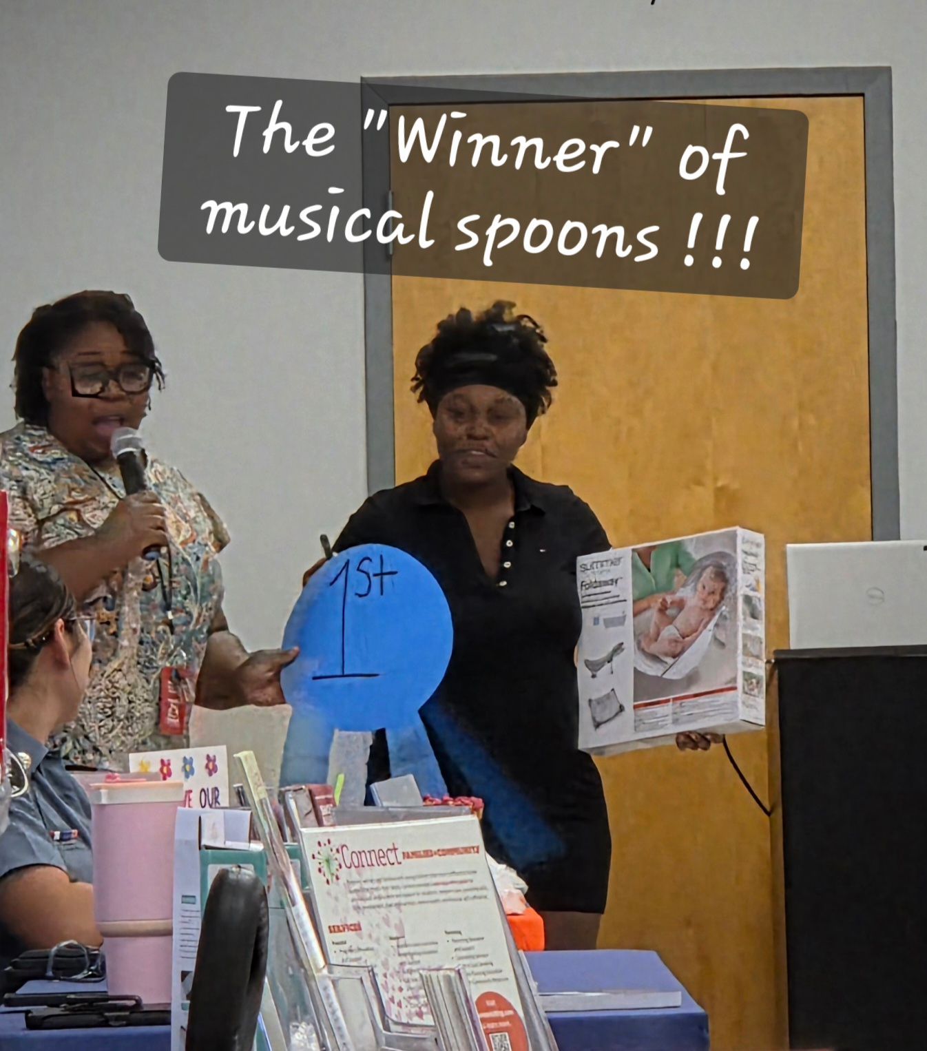Award display for “The Winner of musical spoons,” with two people standing beside it in a classroom.