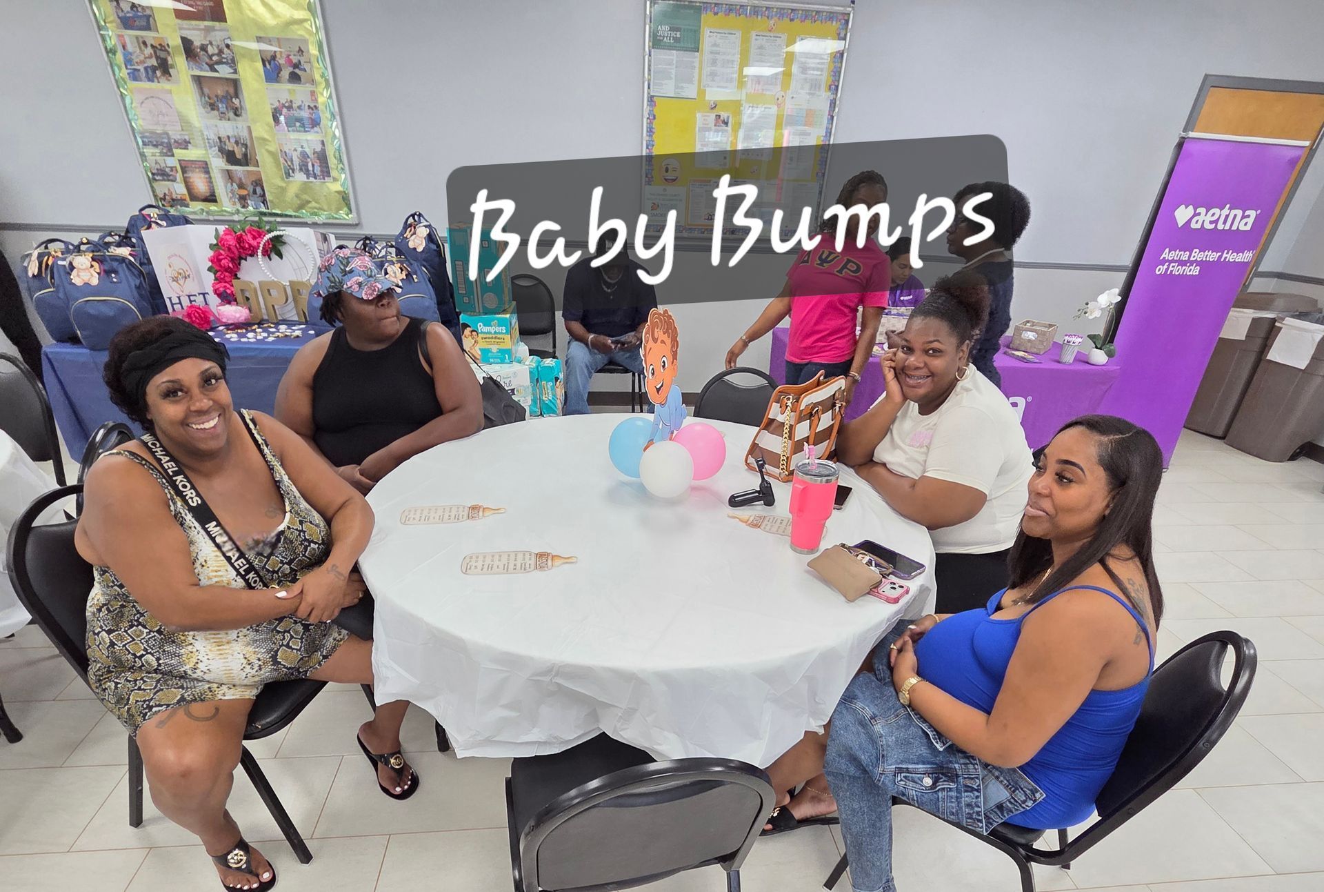 Four people seated at a round table beneath a “Baby Bumps” sign in a bright event room.