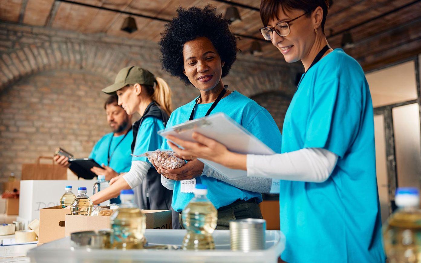 Volunteers sorting donations in a warehouse, wearing matching blue shirts. Two women review a clipboard.