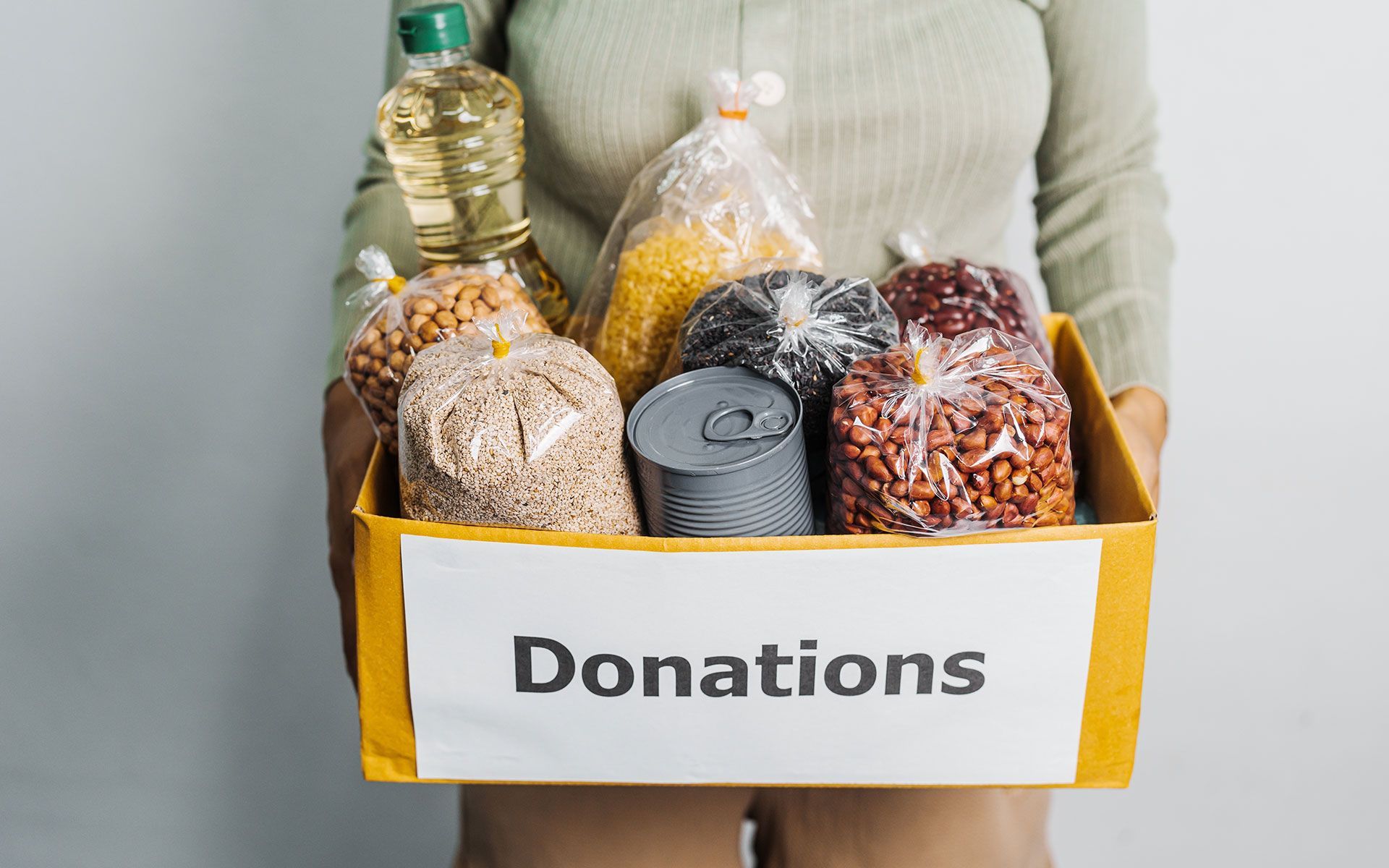Person holding a donation box filled with food items: oil, grains, beans, and canned goods.