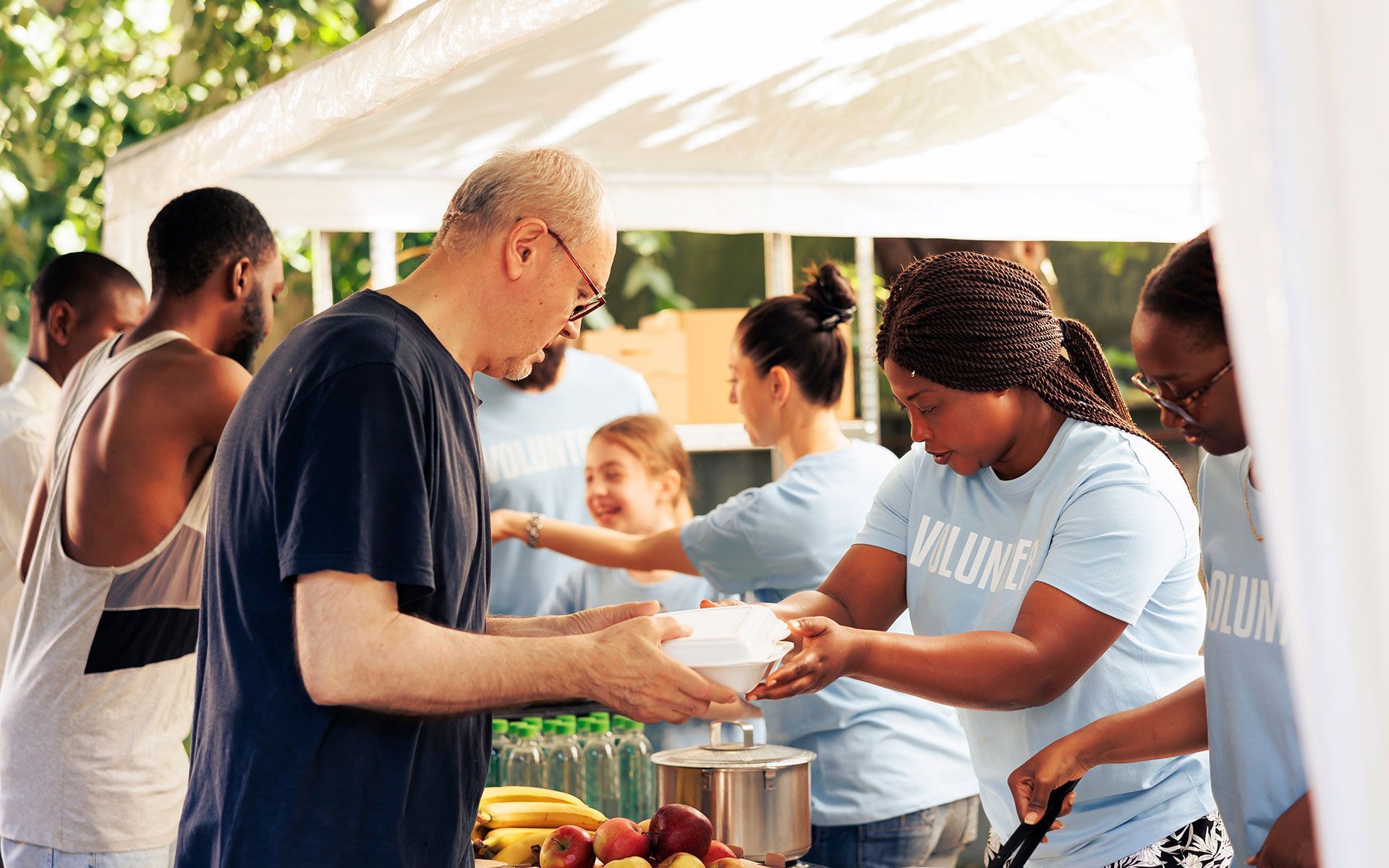 People serving food at an outdoor volunteer event, sunny day.