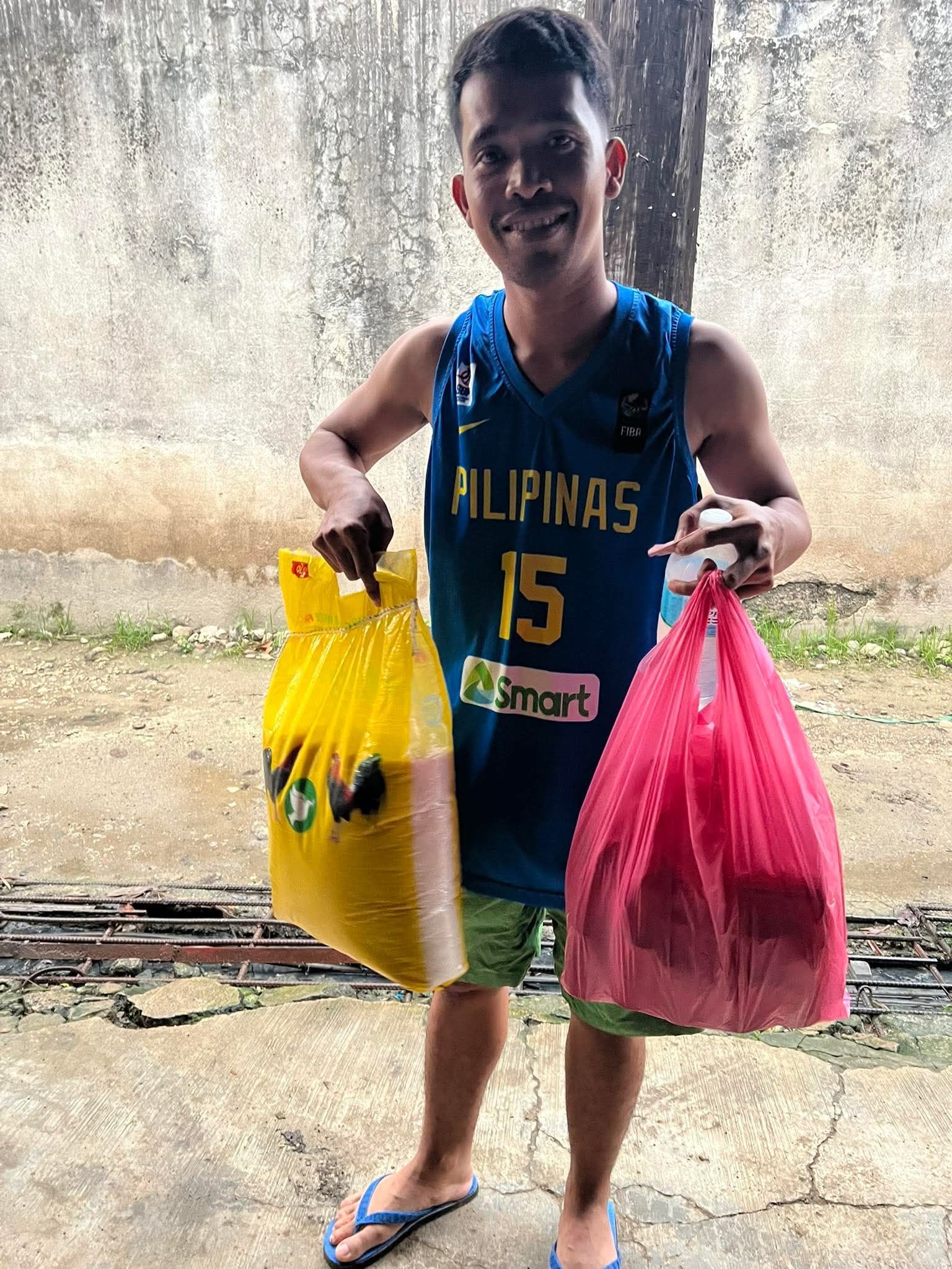 Boy in a blue shirt smiling and holding yellow and pink plastic bags outdoors. | Redhawk Auto Service - Temecula