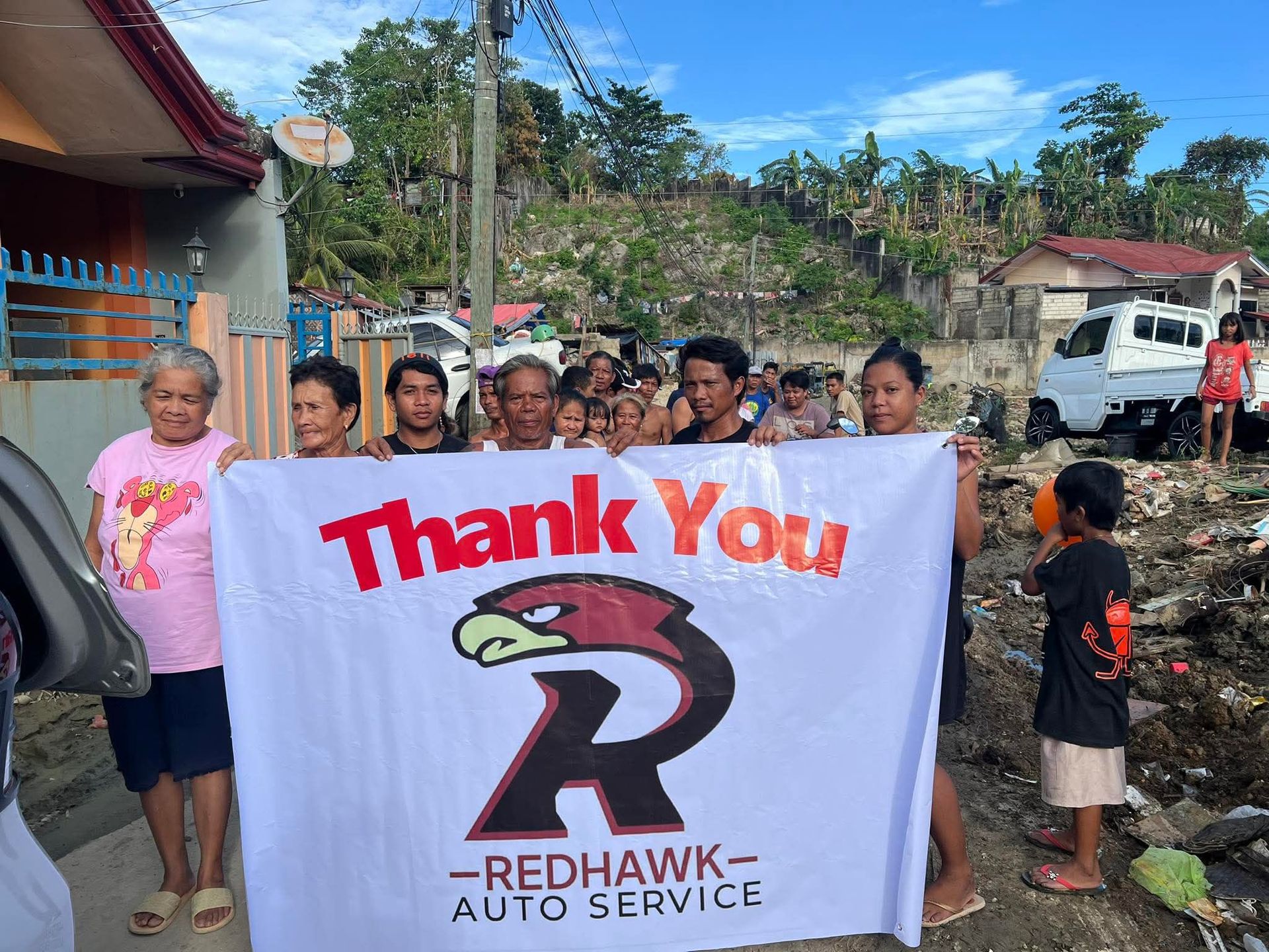 People holding a “Thank You” Red Hawk Auto Service banner outdoors near a truck | Redhawk Auto Service - Temecula