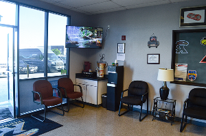 Small office waiting area with chairs, desk, TV, and large windows overlooking a parking lot | Redhawk Auto Service - Temecula