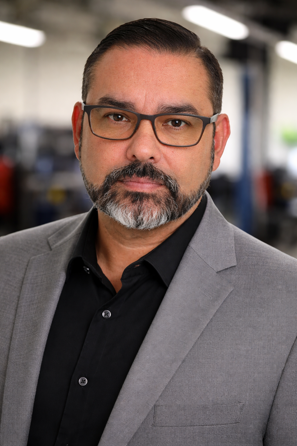 Portrait of a man with glasses and gray blazer against a blurred office background | Redhawk Auto Service - Temecula