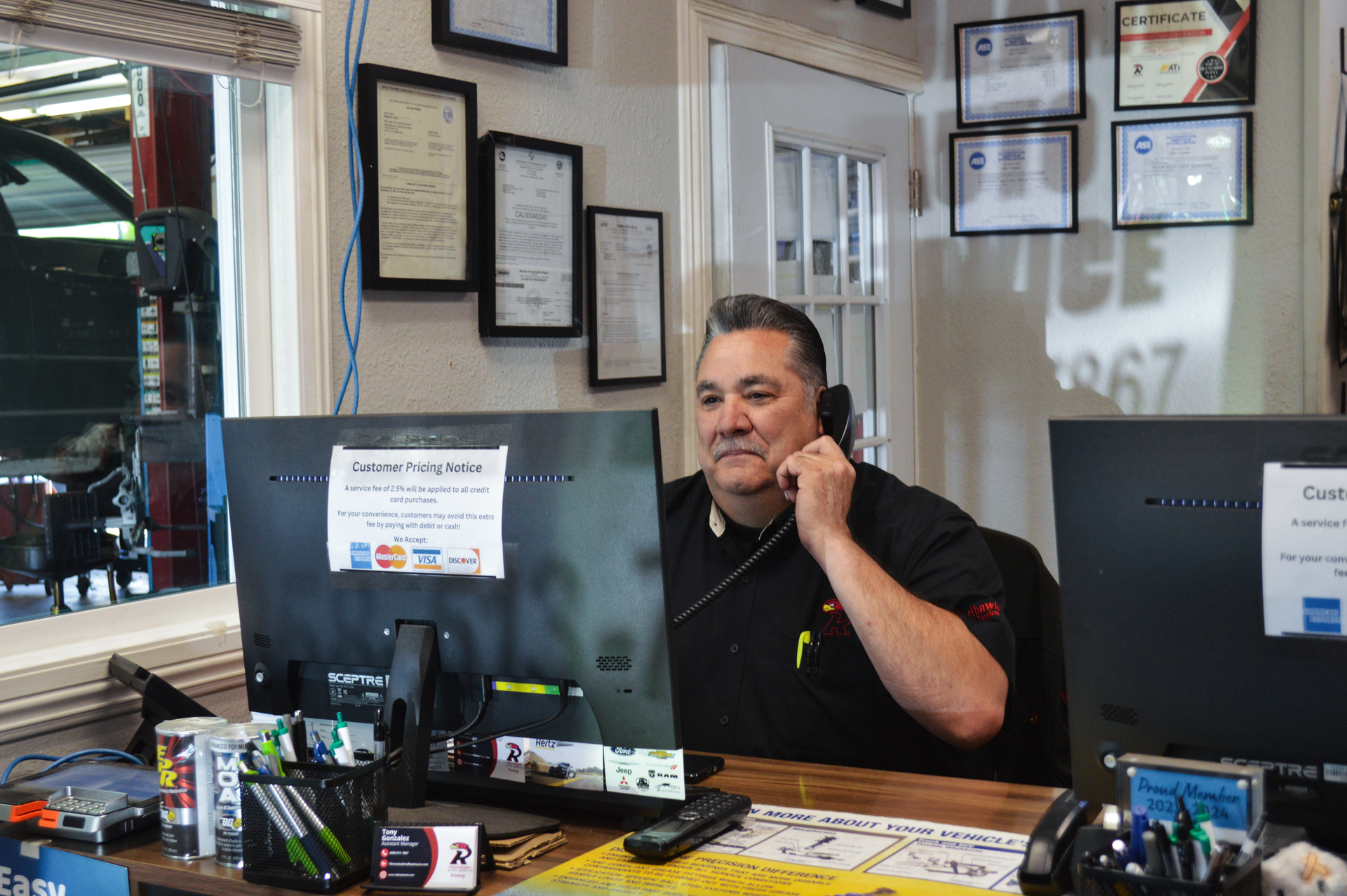 Man on the phone behind a shop counter with framed certificates and computer monitors | Redhawk Auto Service - Temecula
