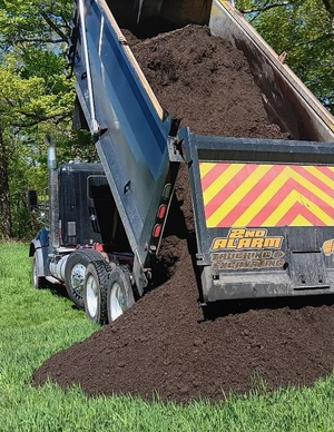 Dump truck unloading dark soil onto the ground outdoors