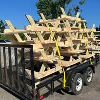 Trailer loaded with stacked wooden racks and secured by a yellow strap outdoors