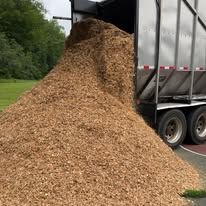 Large pile of wood chips spilled beside a gray dump trailer on a roadside