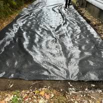 Black plastic mulch covering a garden bed, with a person standing at the top edge