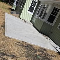 Concrete patio slab beside a light green house with white trim and windows, viewed at an angle