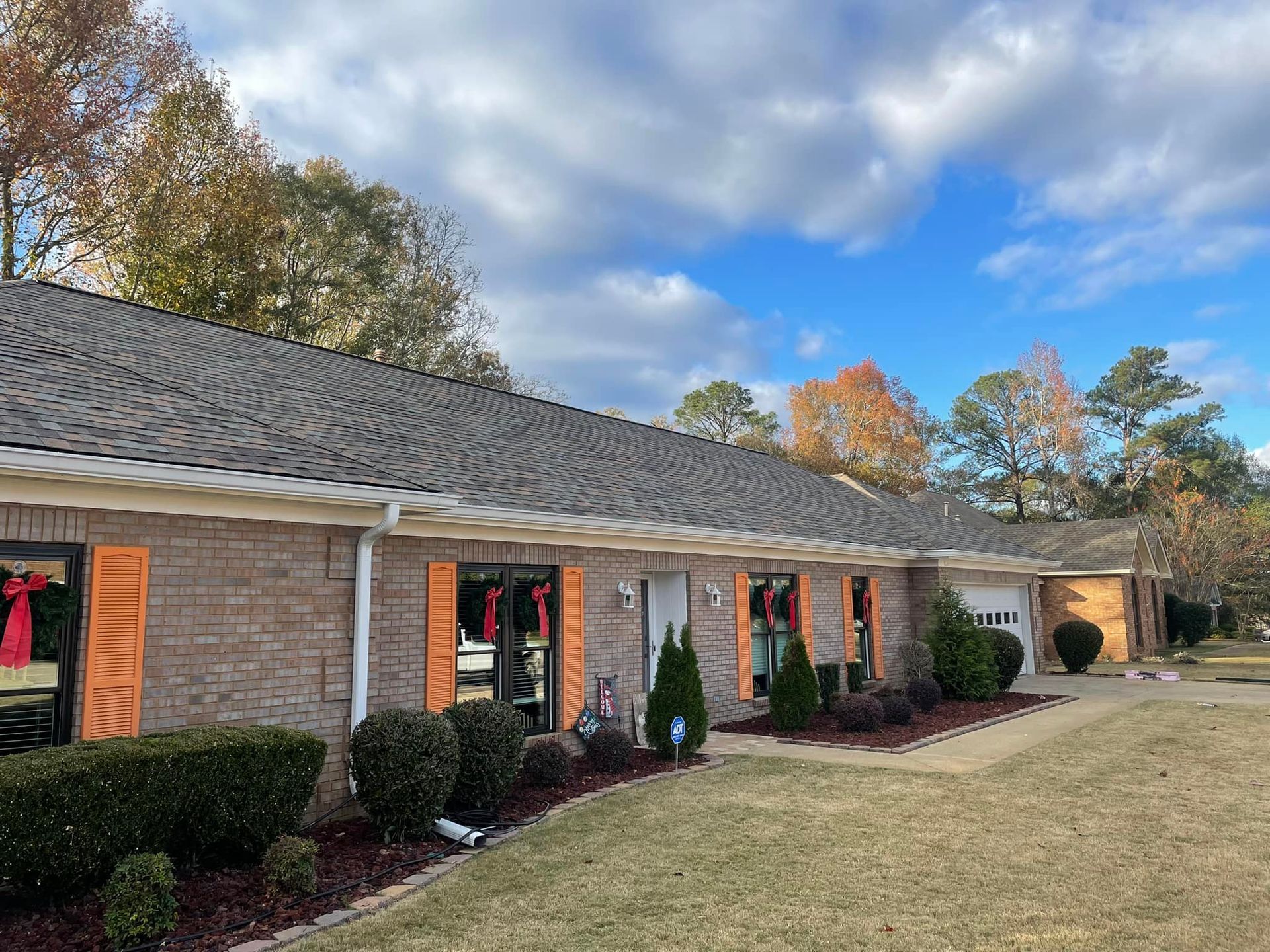 A brick house with a gray roof and orange shutters is decorated for christmas.