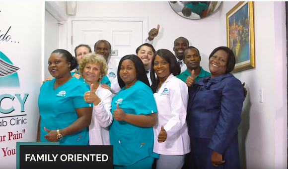 Group of people in scrubs and professional attire, smiling and giving thumbs up. Office setting.