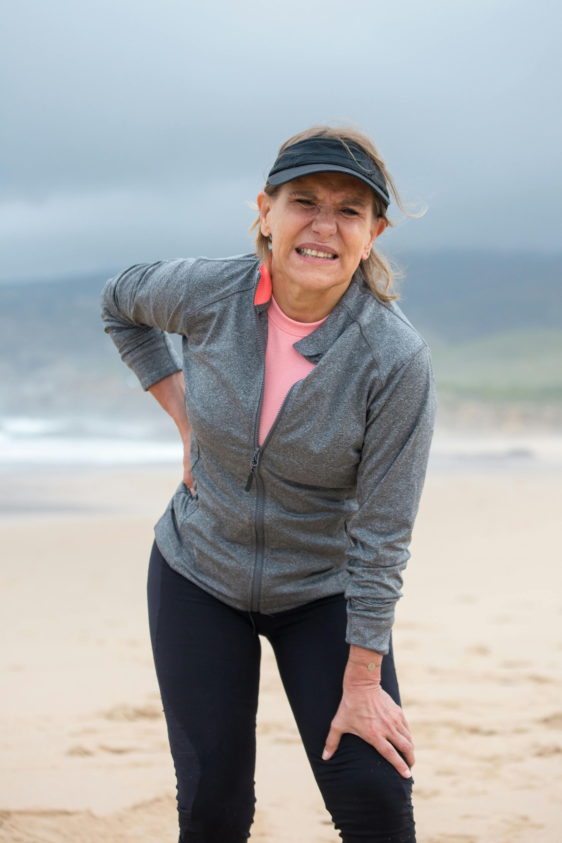 Woman on a beach, holding her knee and back in pain. 