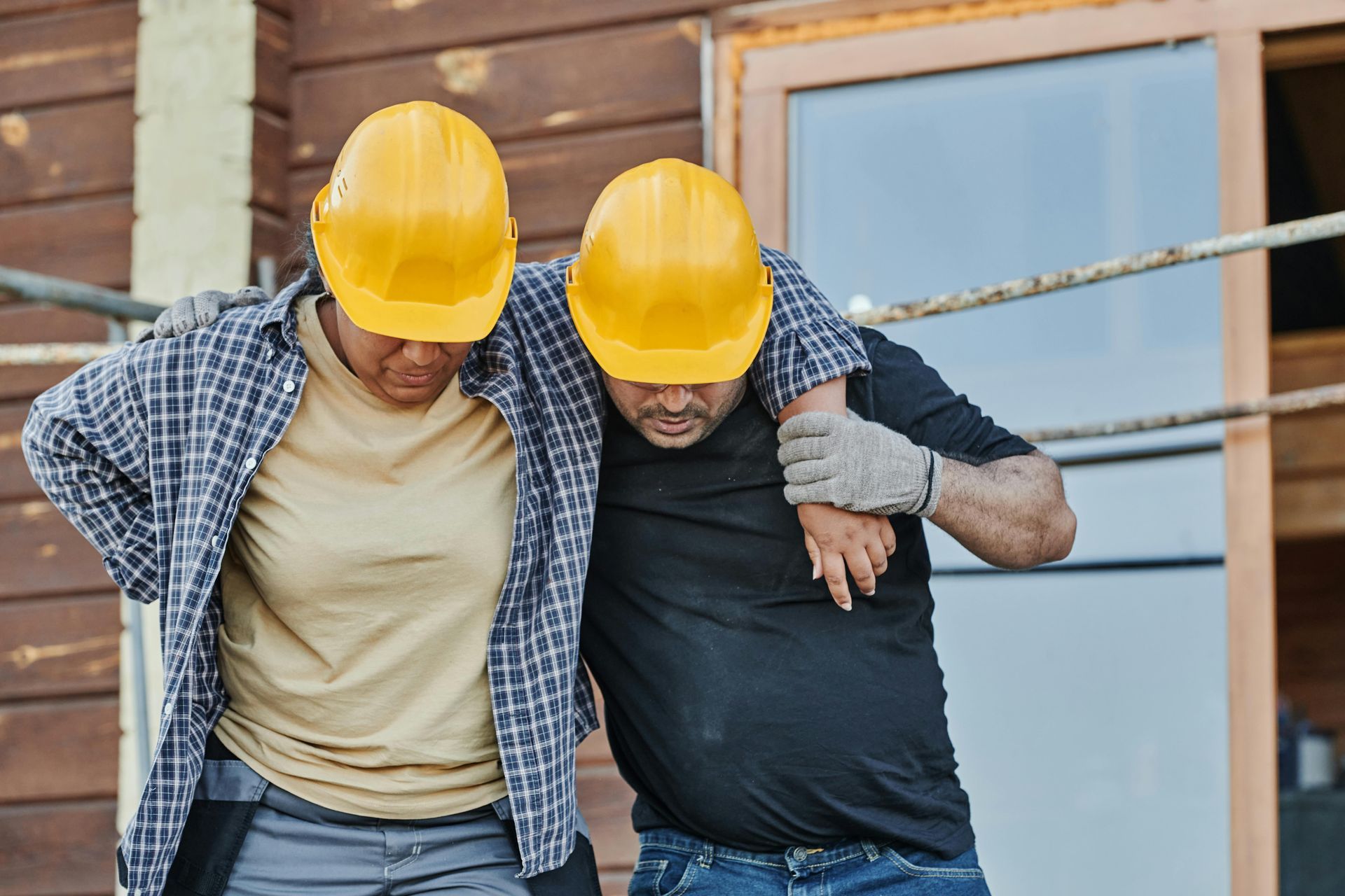 Two construction workers, wearing yellow hard hats, help each other.