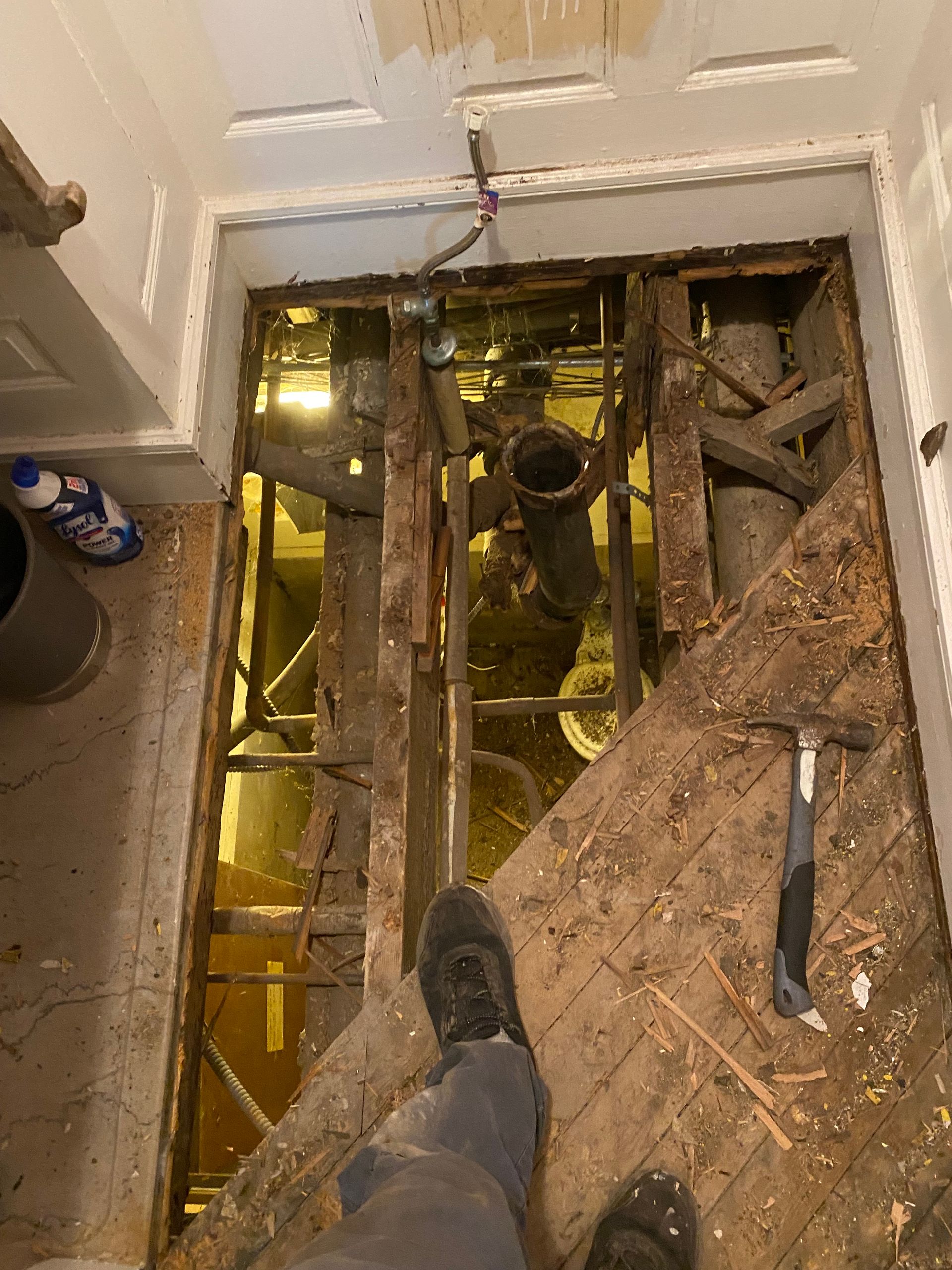 Person standing on exposed floor joists over a yellow-lit crawlspace during renovation