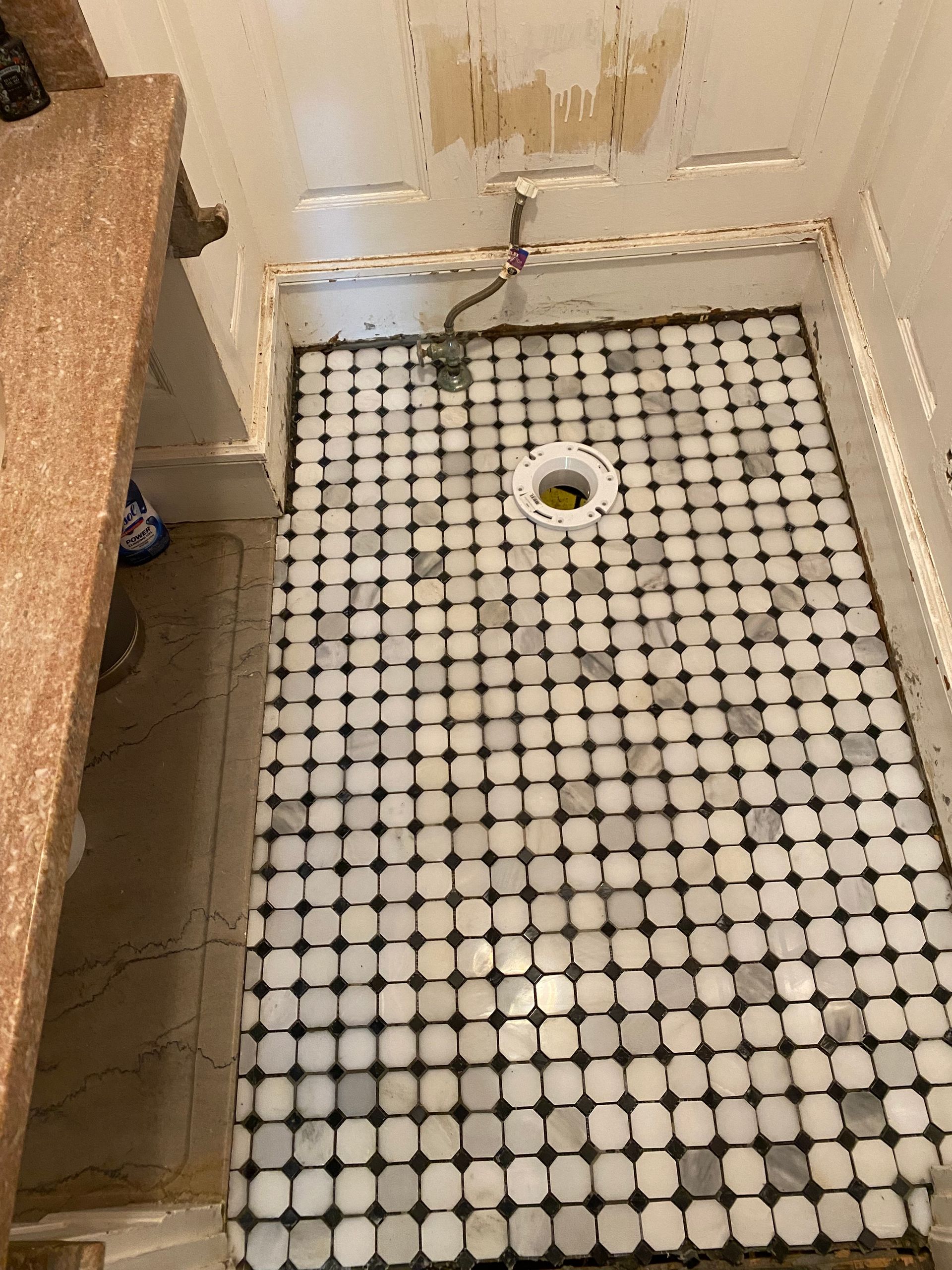 Small bathroom shower floor with black-and-white mosaic tile and a central drain.