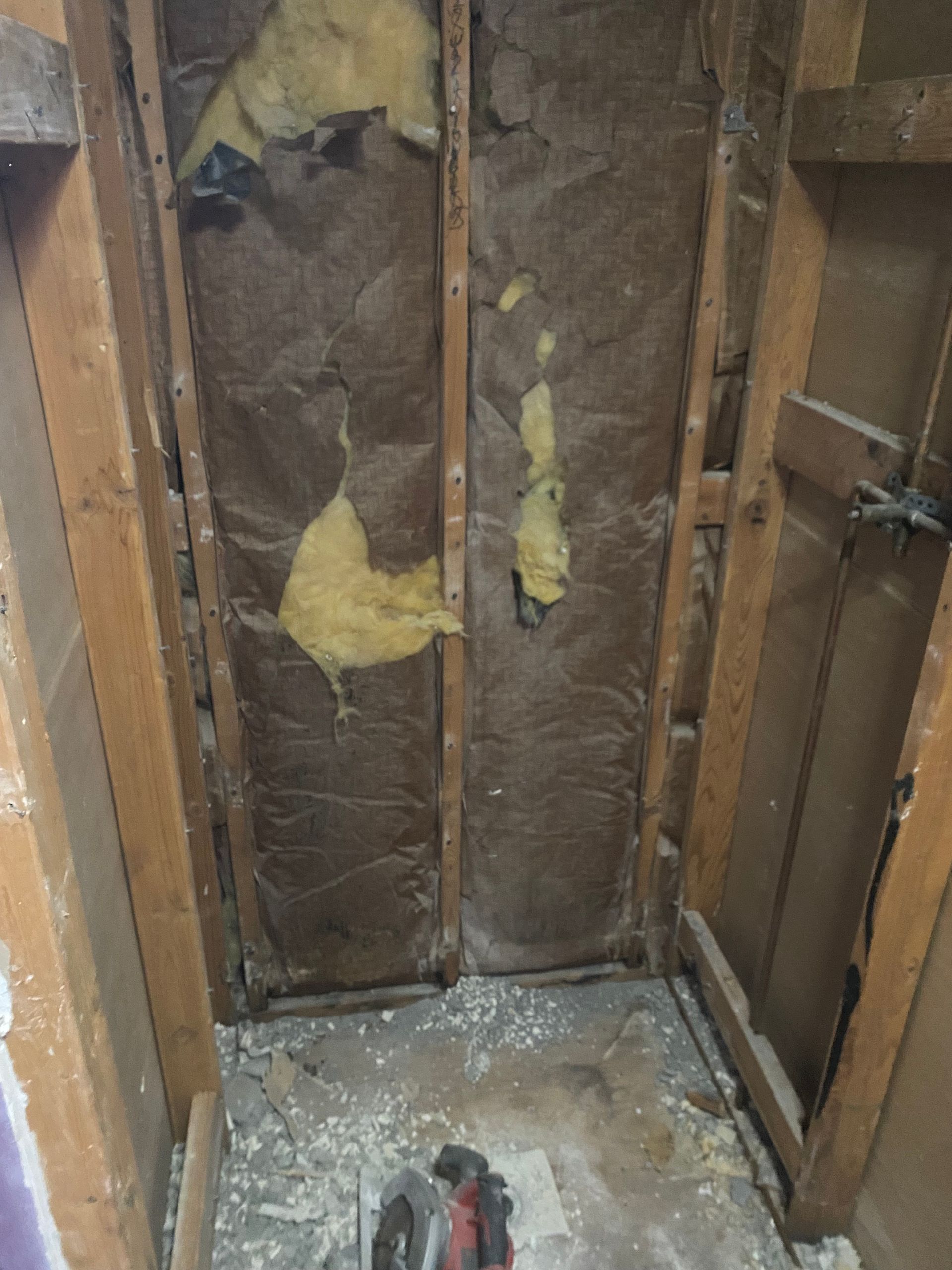 Open wall cavity with exposed insulation and wiring in a small unfinished room