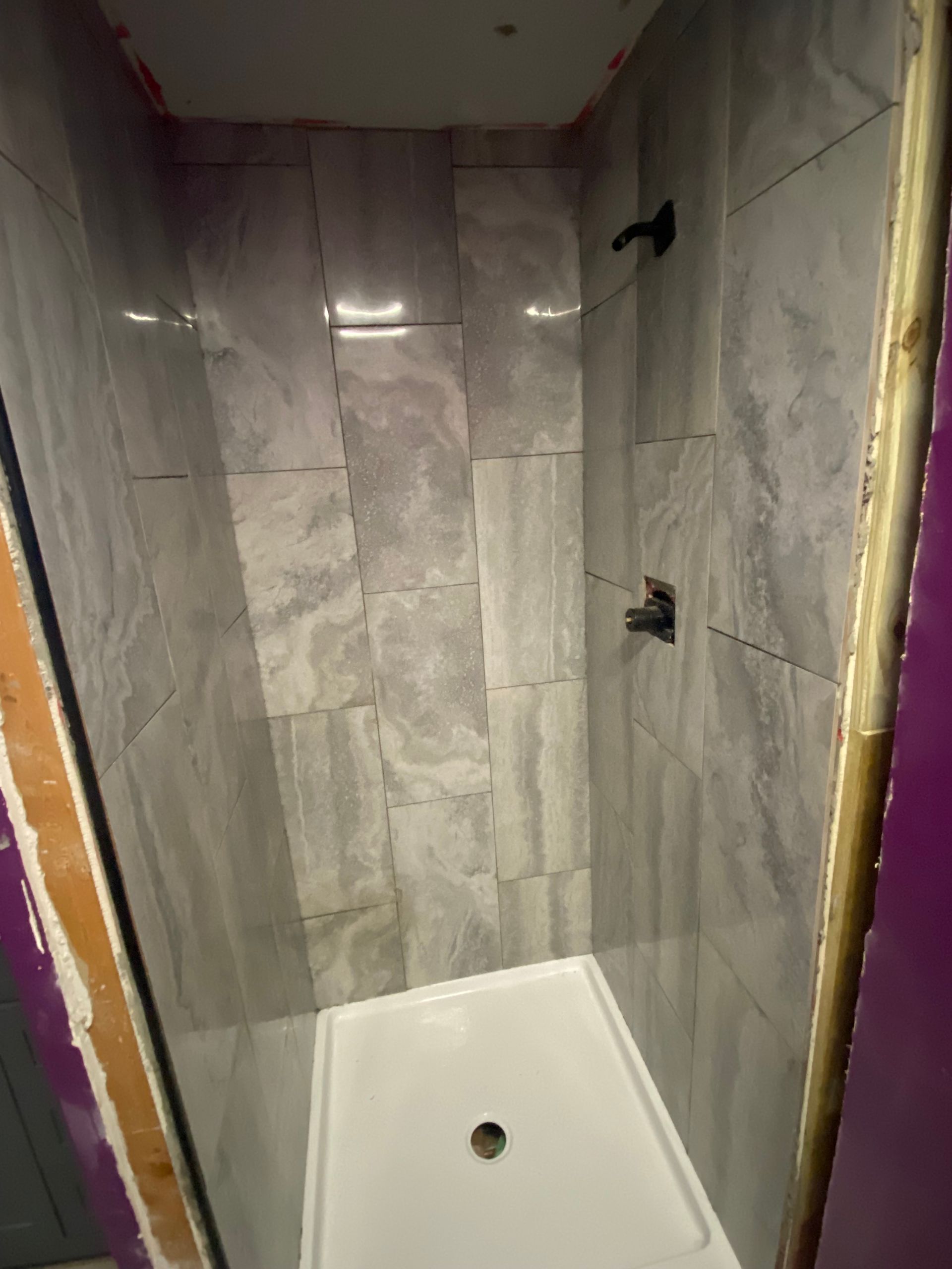 Empty tiled shower stall with white shower pan and black fixtures