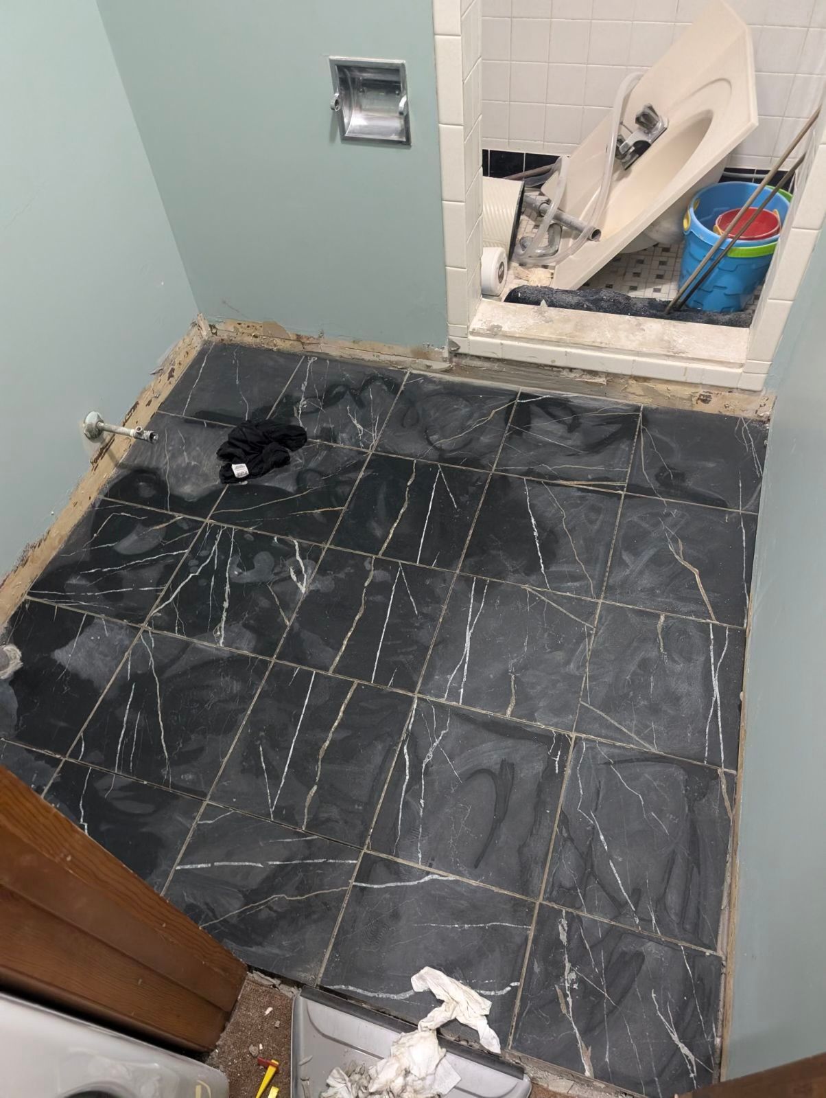 Small bathroom under renovation with dark tile floor, open wall access, and scattered tools and debris