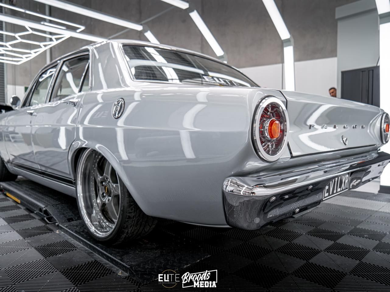 Classic gray Ford sedan on display, shiny chrome wheels, in a bright showroom.