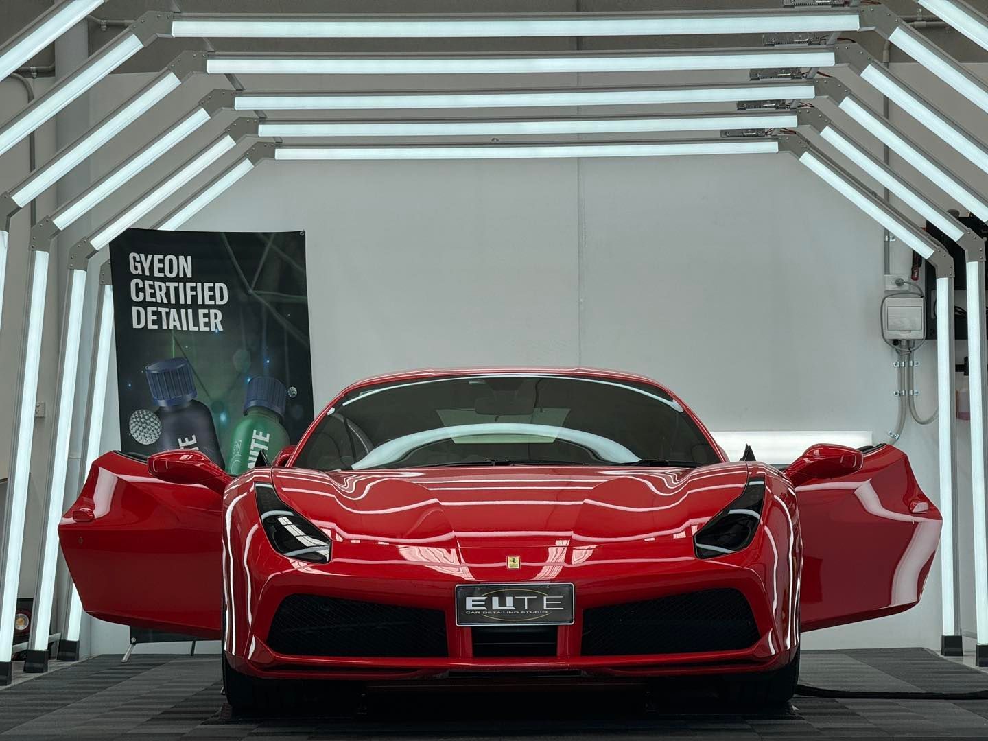 Red Ferrari sports car with open doors, inside a detail shop.