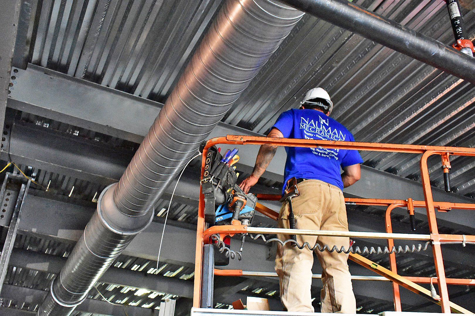 A man is standing on a scaffolding working on a pipe.