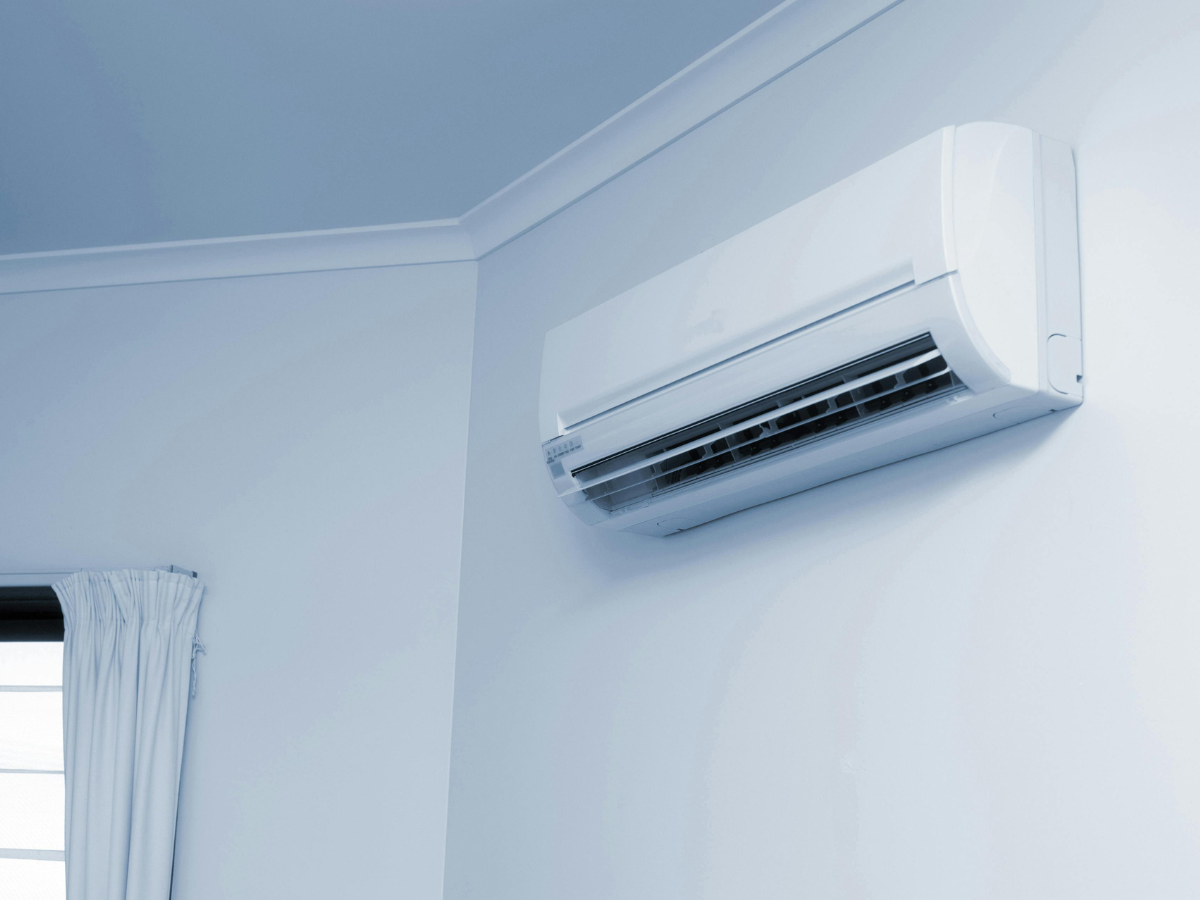 A white air conditioner is mounted on a white wall next to a window.