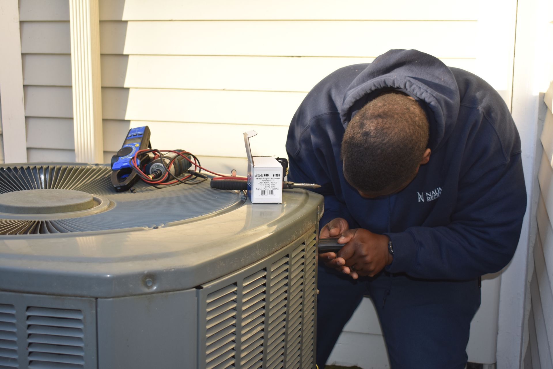 A worker from Nauman Inc. is working on an air conditioner outside of a house.