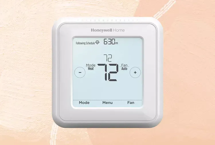 A white thermostat is sitting on a pink surface.